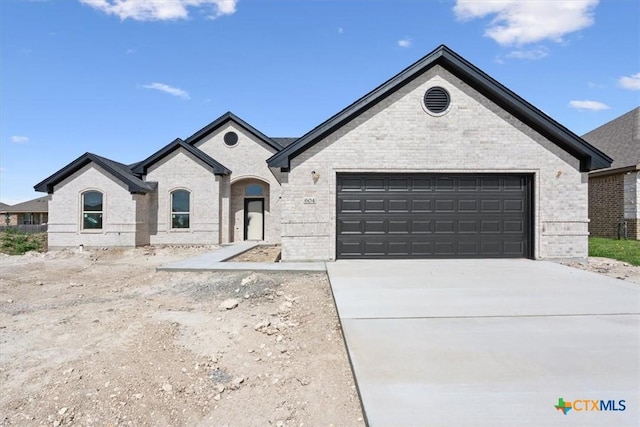 french country inspired facade featuring brick siding, concrete driveway, and a garage