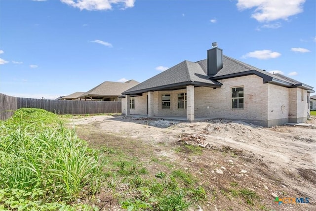 back of property featuring fence, a chimney, brick siding, and roof with shingles