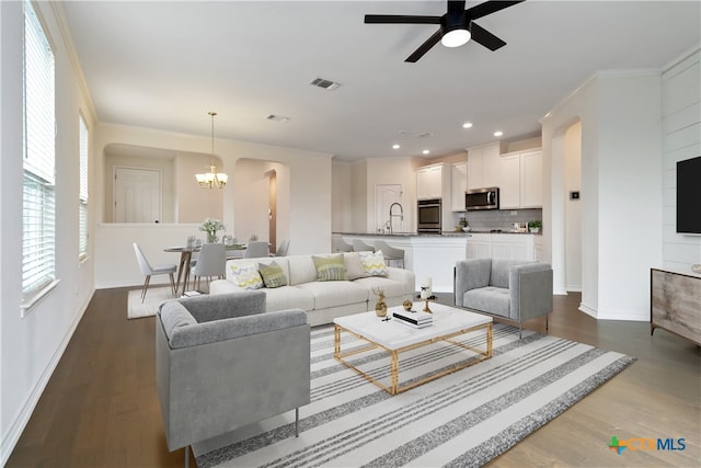 living room featuring ceiling fan with notable chandelier, dark wood-type flooring, sink, and crown molding