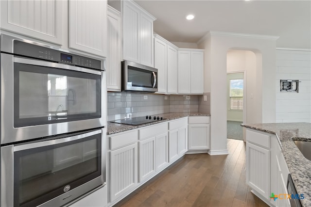 kitchen with appliances with stainless steel finishes, light stone countertops, crown molding, white cabinets, and dark wood-type flooring