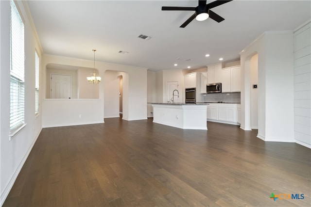 unfurnished living room with dark wood-type flooring, ceiling fan with notable chandelier, sink, and ornamental molding