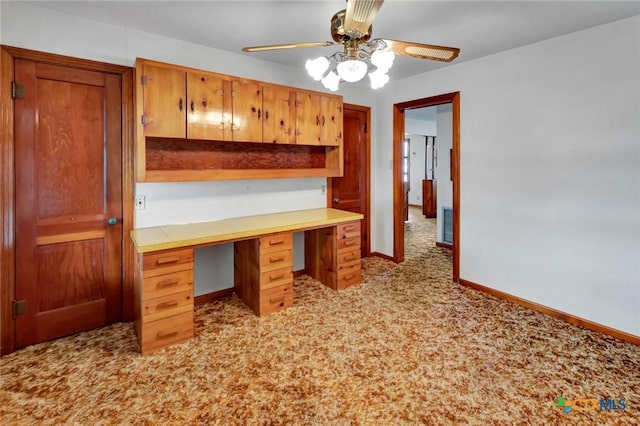 kitchen with built in desk, light colored carpet, and ceiling fan