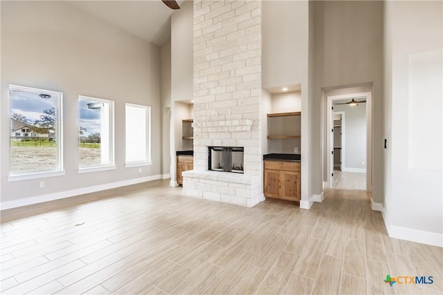 unfurnished living room with a stone fireplace, ceiling fan, a towering ceiling, and light wood-type flooring