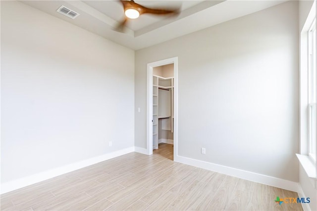 spare room featuring a raised ceiling, ceiling fan, and light hardwood / wood-style flooring