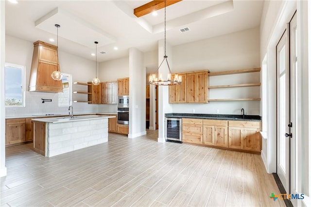 kitchen featuring pendant lighting, a kitchen island with sink, a raised ceiling, wine cooler, and appliances with stainless steel finishes