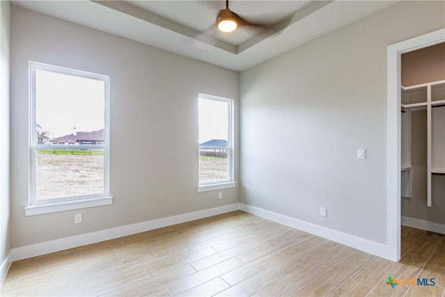 unfurnished bedroom featuring a tray ceiling, a spacious closet, ceiling fan, and light hardwood / wood-style floors