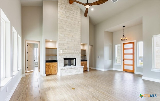 unfurnished living room featuring beam ceiling, high vaulted ceiling, ceiling fan, and a stone fireplace