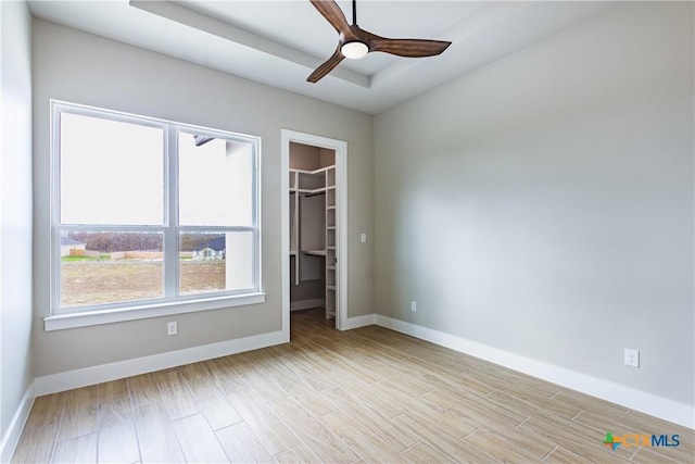 unfurnished bedroom featuring a raised ceiling, ceiling fan, a spacious closet, light hardwood / wood-style floors, and a closet