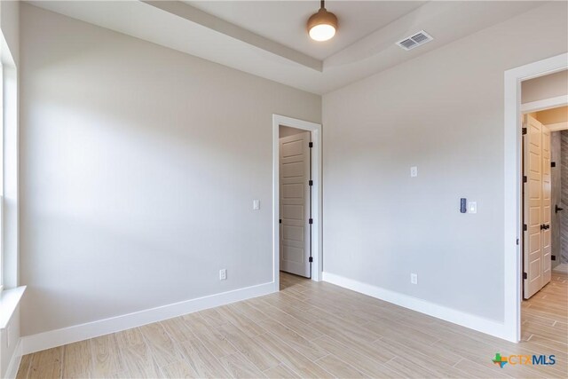 unfurnished room featuring a tray ceiling and light hardwood / wood-style flooring