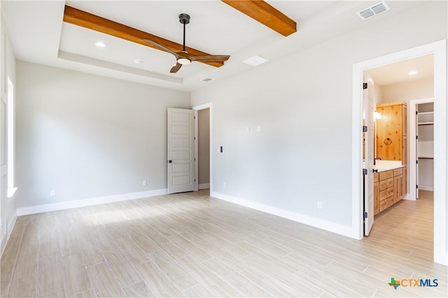 empty room with ceiling fan, light wood-type flooring, and a tray ceiling