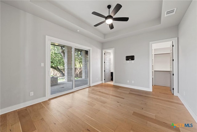 unfurnished bedroom with access to exterior, ceiling fan, a closet, a walk in closet, and a tray ceiling