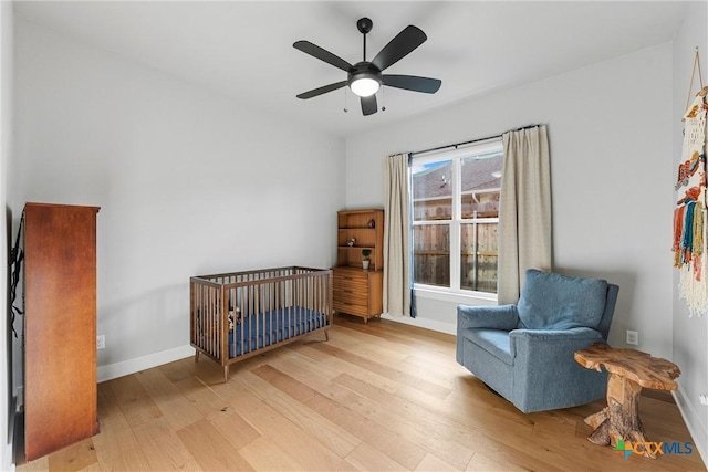 bedroom featuring ceiling fan, light hardwood / wood-style flooring, and a nursery area