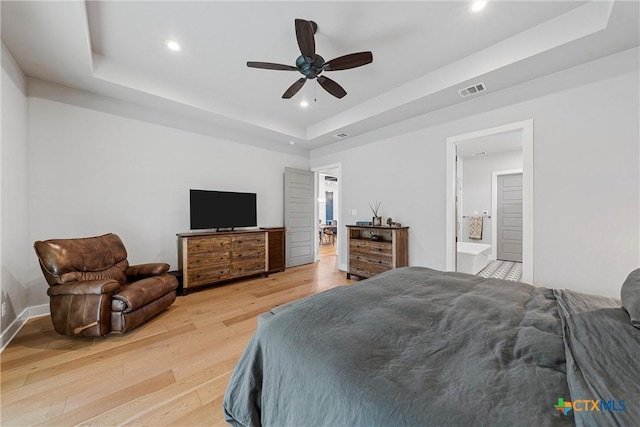 bedroom featuring ceiling fan, a tray ceiling, light hardwood / wood-style flooring, and connected bathroom