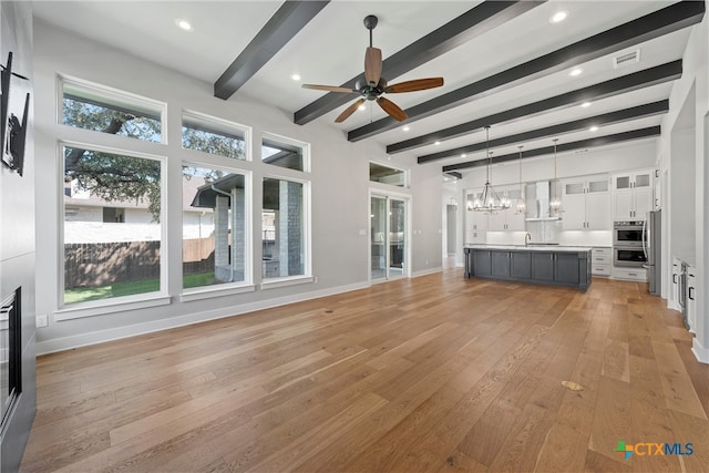 unfurnished living room with a wealth of natural light, light hardwood / wood-style flooring, beamed ceiling, and sink