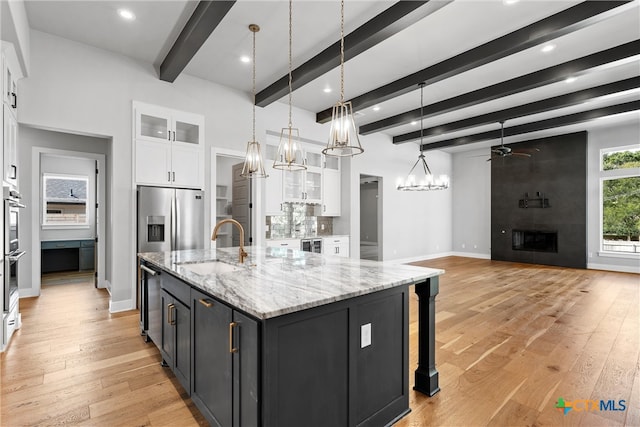 kitchen featuring pendant lighting, beam ceiling, ceiling fan with notable chandelier, a large island with sink, and white cabinetry