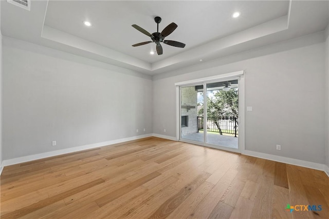 unfurnished room featuring a large fireplace, ceiling fan, a tray ceiling, and light hardwood / wood-style flooring