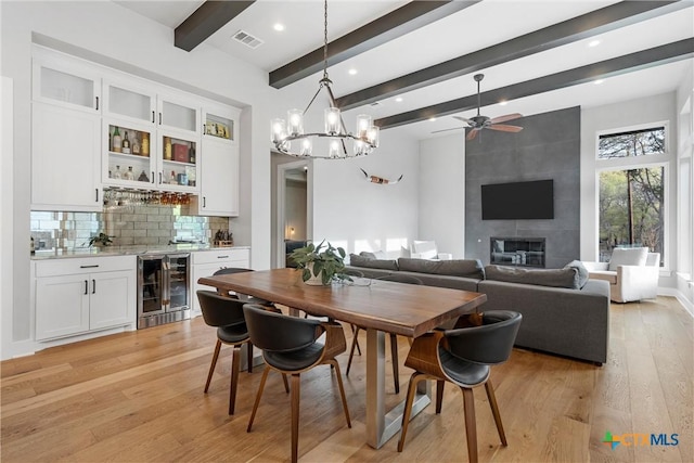 dining space with light hardwood / wood-style floors, beam ceiling, wine cooler, a tiled fireplace, and ceiling fan