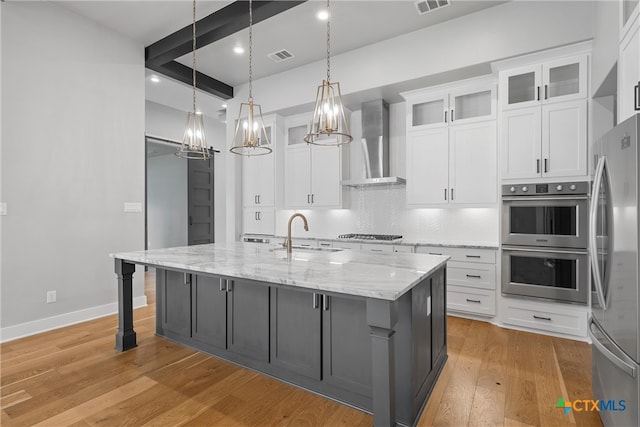 kitchen featuring stainless steel appliances, a kitchen island with sink, wall chimney exhaust hood, and white cabinets