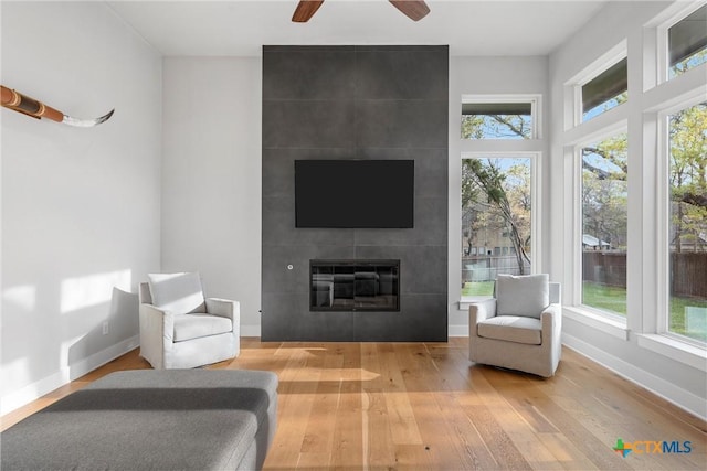 living area with a tiled fireplace, ceiling fan, and hardwood / wood-style floors