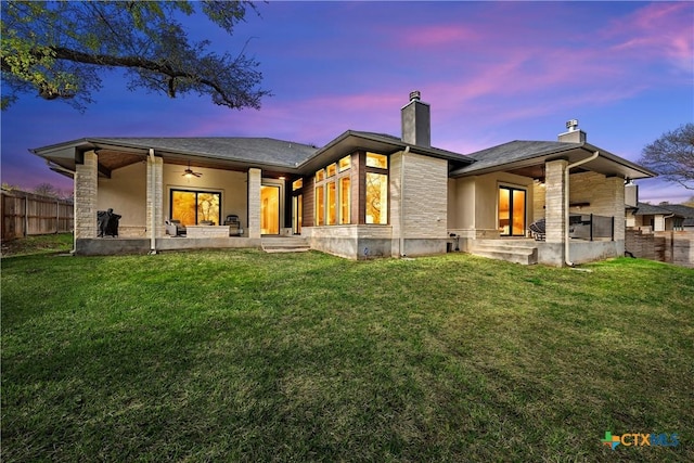 back house at dusk with a patio, ceiling fan, and a yard