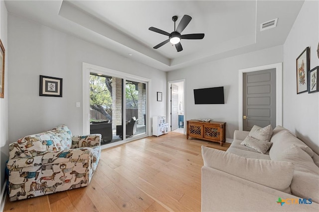 living room with a raised ceiling, ceiling fan, and light hardwood / wood-style flooring