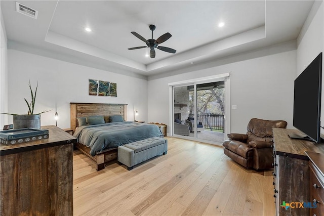 bedroom featuring ceiling fan, light hardwood / wood-style flooring, access to exterior, and a tray ceiling