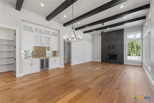 unfurnished living room with a tile fireplace, beamed ceiling, light hardwood / wood-style flooring, ceiling fan with notable chandelier, and wine cooler