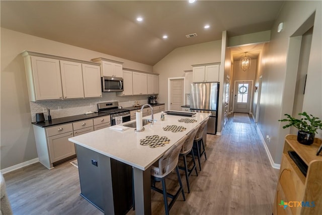 kitchen featuring visible vents, a kitchen island with sink, a sink, appliances with stainless steel finishes, and a kitchen bar