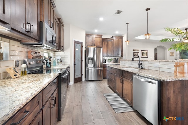 kitchen with a sink, tasteful backsplash, light wood-style floors, and appliances with stainless steel finishes