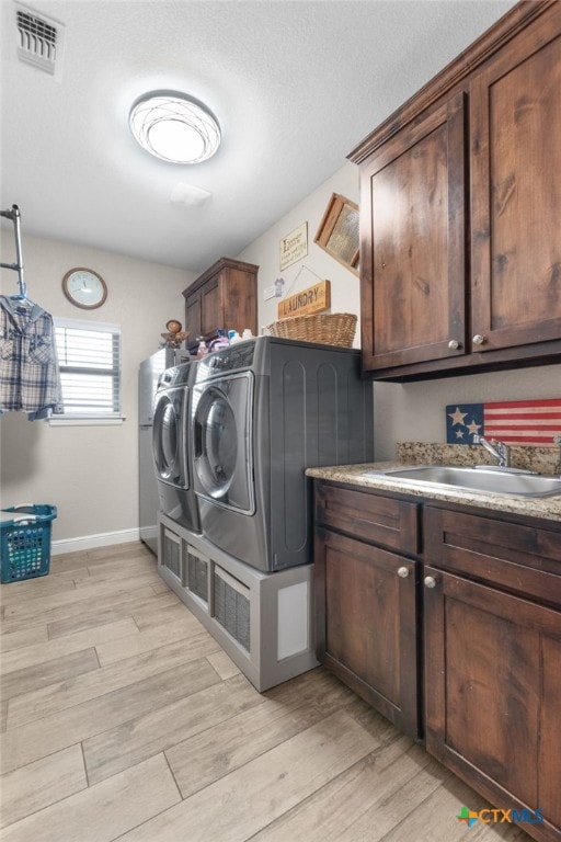 laundry area featuring visible vents, light wood-type flooring, a sink, cabinet space, and separate washer and dryer