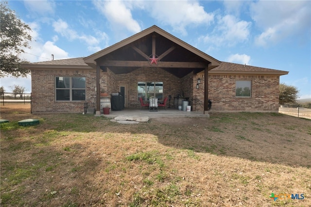 back of property with a yard, brick siding, a patio, and fence