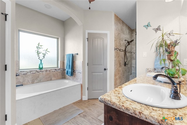 bathroom with a garden tub, double vanity, a tile shower, wood finished floors, and a sink