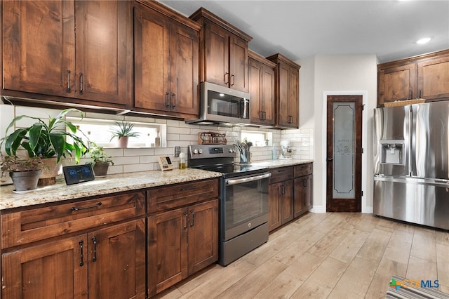 kitchen with light wood-style flooring, backsplash, light stone countertops, and appliances with stainless steel finishes