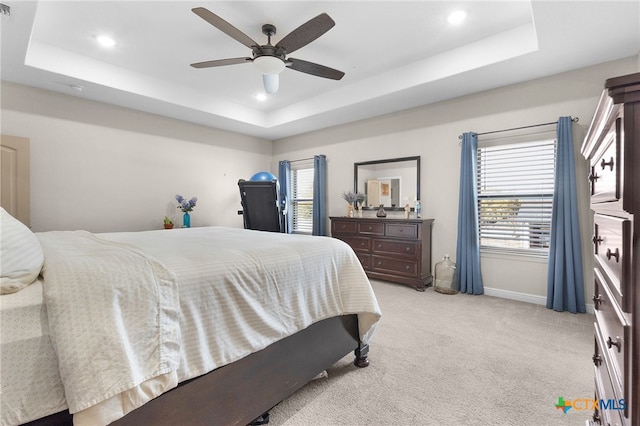 bedroom featuring a tray ceiling, multiple windows, light colored carpet, and baseboards