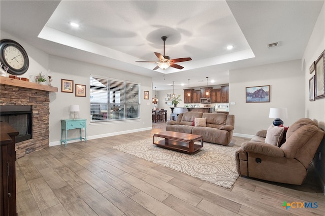 living area with a fireplace, a raised ceiling, baseboards, and wood finished floors