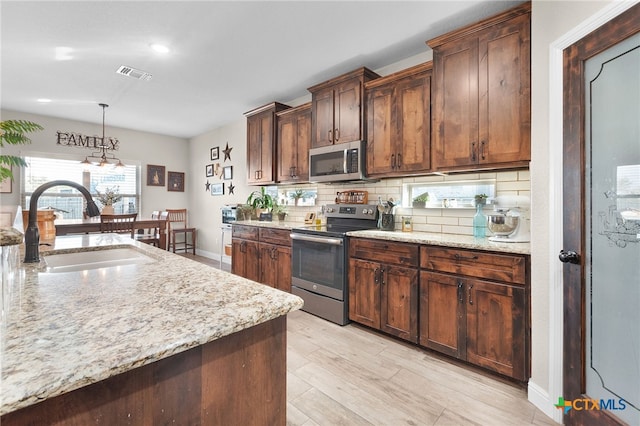 kitchen with a sink, stainless steel appliances, light stone counters, and tasteful backsplash