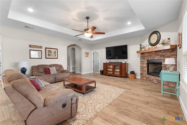 living area featuring light wood-type flooring, visible vents, a raised ceiling, and arched walkways