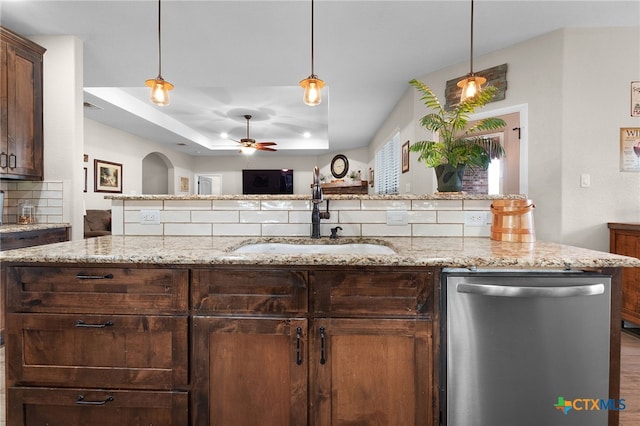 kitchen with a sink, dark brown cabinetry, stainless steel dishwasher, a raised ceiling, and backsplash