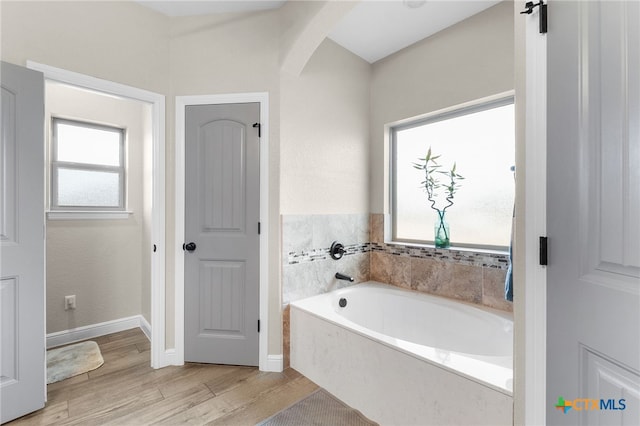 bathroom featuring baseboards, wood finished floors, and a bath