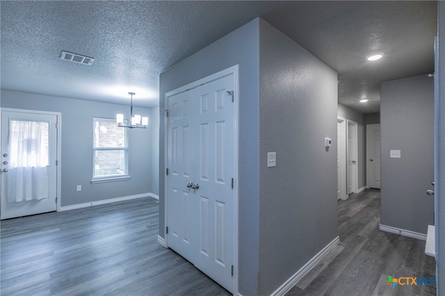 hall with dark hardwood / wood-style flooring, a textured ceiling, and an inviting chandelier