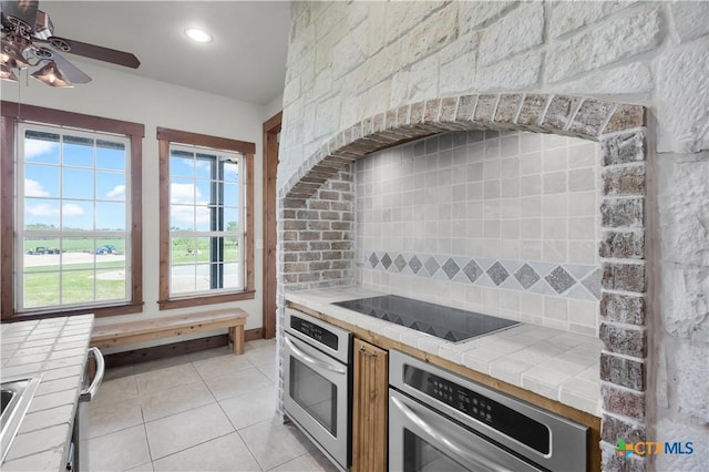 12491 Madison Ln, Justin, TX 76247 - kitchen with stainless steel oven, tile counters, black electric cooktop, and light tile patterned floors