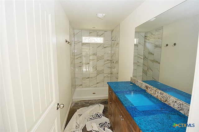 bathroom with vanity, a tile shower, and a textured ceiling