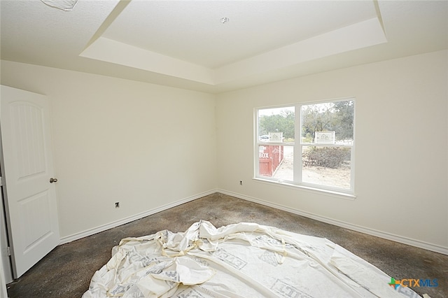 unfurnished room with a tray ceiling and dark colored carpet