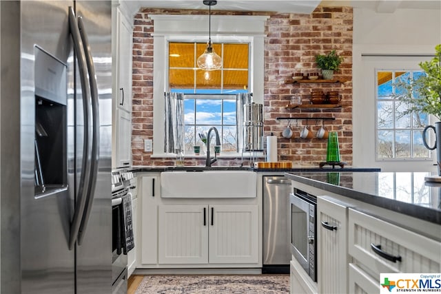 kitchen featuring white cabinetry, sink, appliances with stainless steel finishes, dark stone counters, and decorative light fixtures