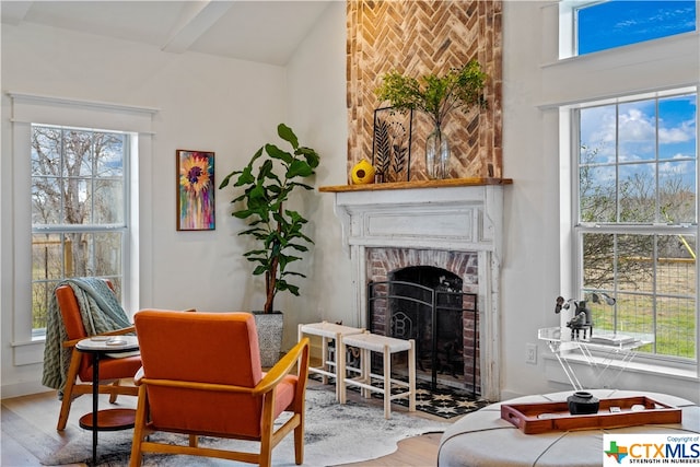 sitting room with a brick fireplace, hardwood / wood-style floors, and lofted ceiling with beams