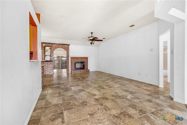 unfurnished living room featuring visible vents, baseboards, a brick fireplace, and a ceiling fan