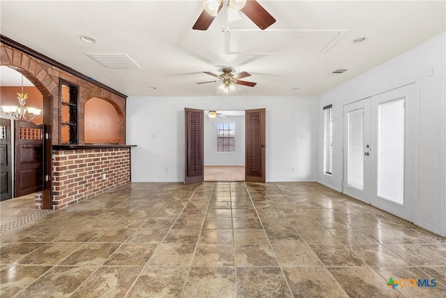 unfurnished living room with visible vents, ceiling fan with notable chandelier, and attic access