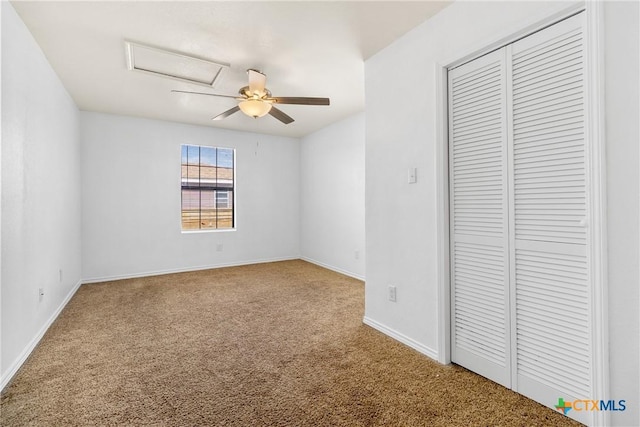 unfurnished bedroom featuring a closet, carpet flooring, baseboards, attic access, and ceiling fan