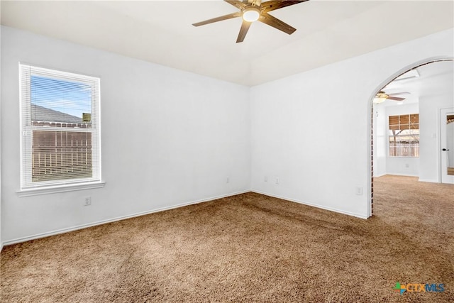 carpeted spare room with arched walkways, baseboards, and a ceiling fan