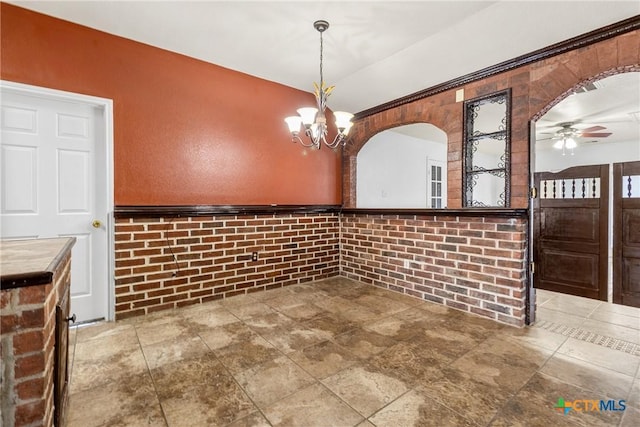 unfurnished dining area featuring arched walkways and ceiling fan with notable chandelier